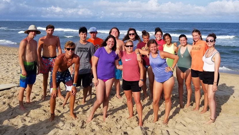 Group of students pose for a picture on a beach in front of water